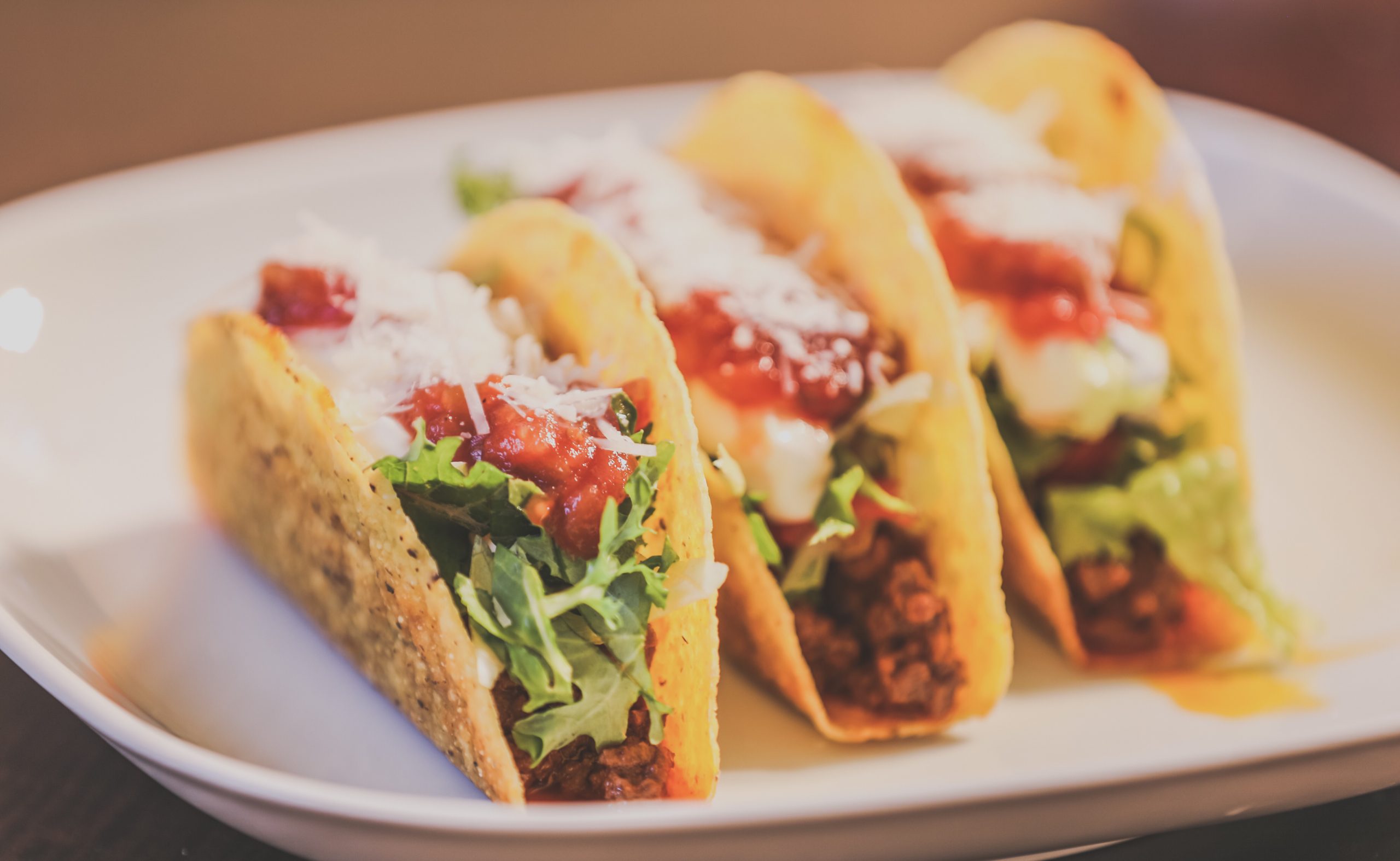 3 homemade tacos lined up on a plain white square plate.